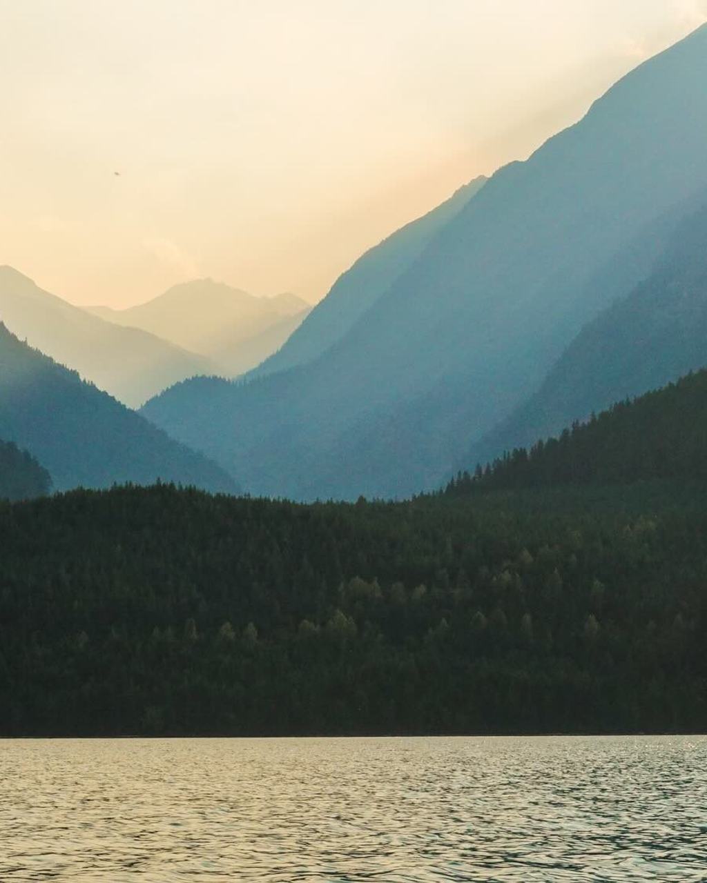 Layered mountain ridges fading into summer haze above a lake